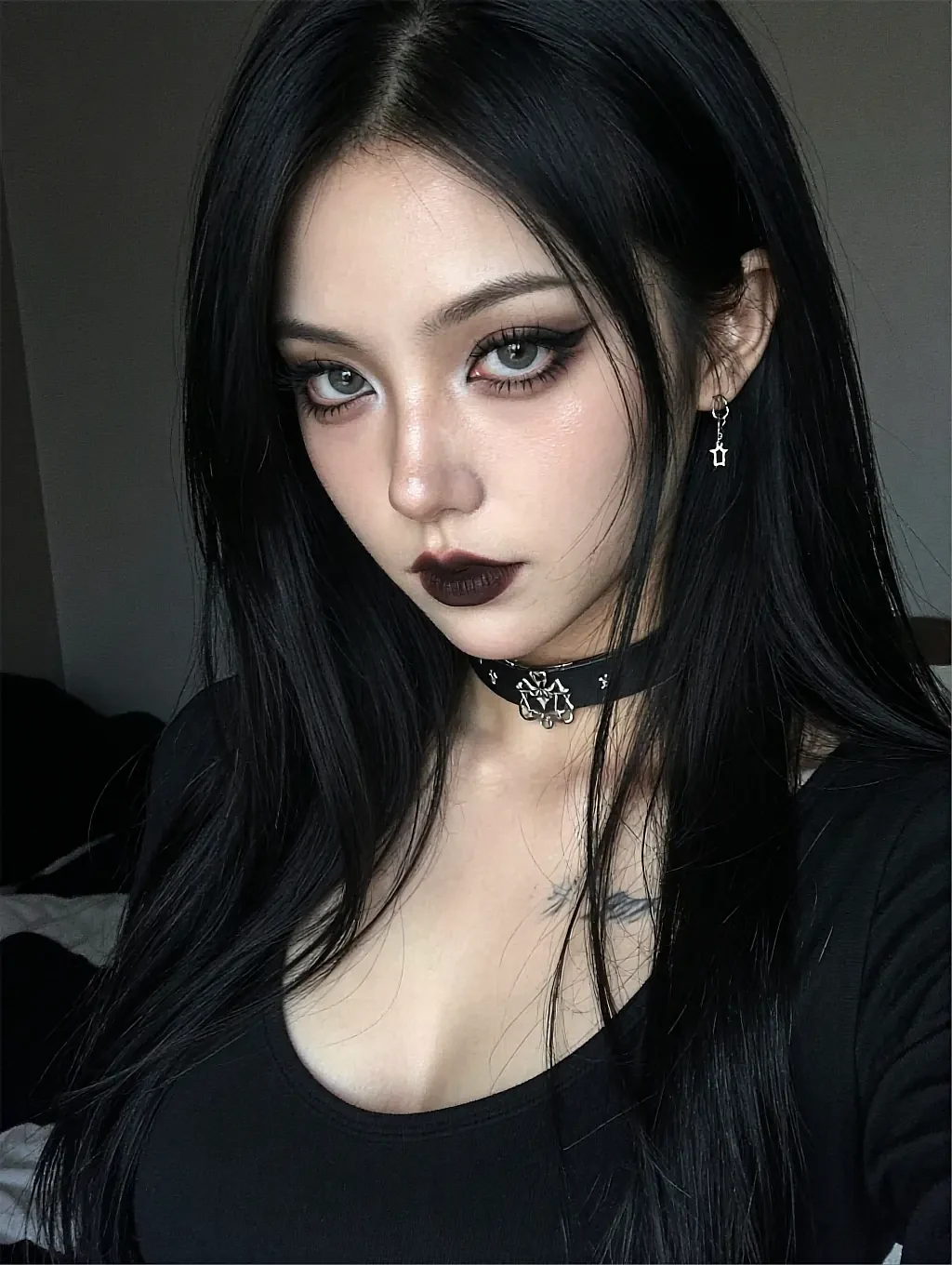 Nadia, a fictional AI character, close up in dark lipstick and a studded black choker, long black hair against a dim wall